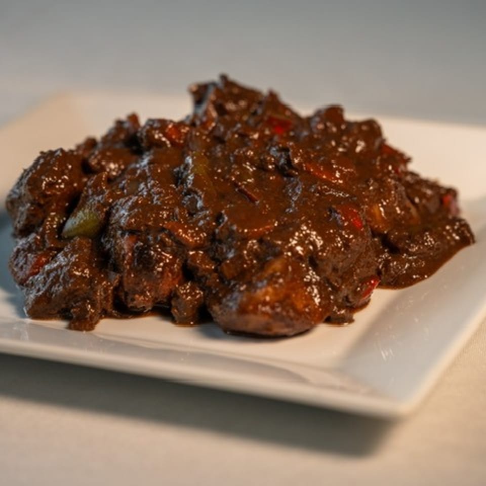 Glazed, richly browned meat pieces with peppers served on a white rectangular plate.