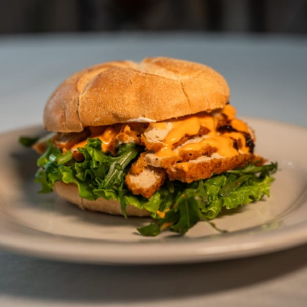 A Caribbean chicken sandwich with lettuce and orange sauce on a white plate.