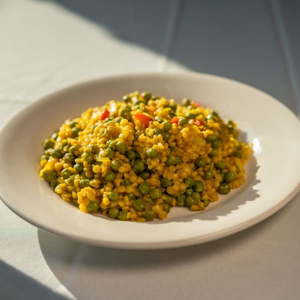 A white plate holds a vibrant Caribbean dish of yellow rice with green peas and red peppers.