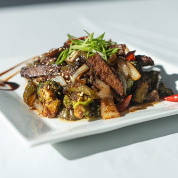Caribbean stir-fry with meat, broccoli, onions, and peppers, garnished with sesame seeds and scallions.