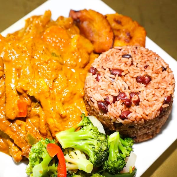 Caribbean dish with chicken in orange sauce, rice and beans, fried plantains, and broccoli.