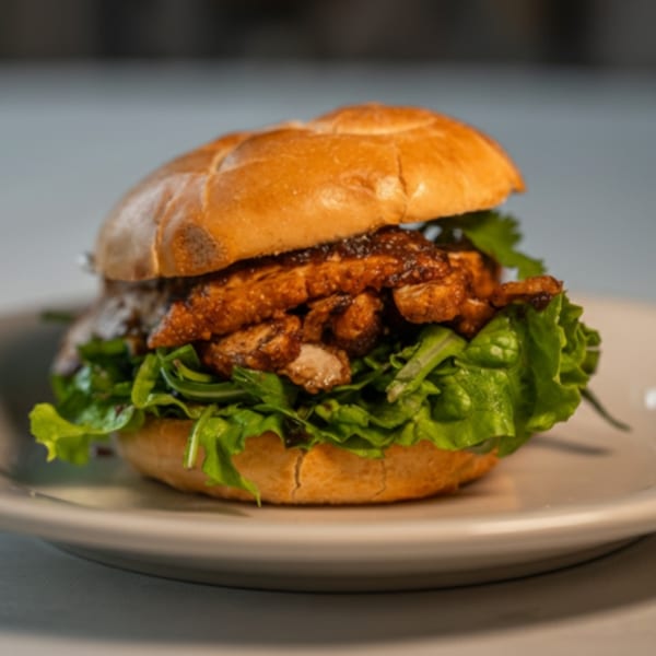 A Caribbean jerk chicken sandwich with lettuce on a bun, served on a white plate.