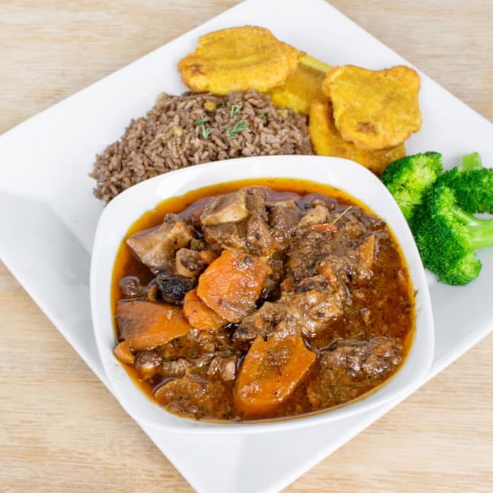 Caribbean stew with meat and carrots, served with rice, fried plantains, and broccoli.