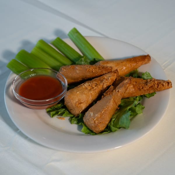 Fried Caribbean fritters on lettuce with celery sticks and a side of dipping sauce.