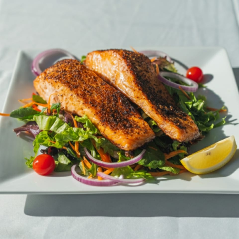 Two seasoned salmon fillets on a bed of fresh greens with cherry tomatoes, red onion, and a lemon wedge.