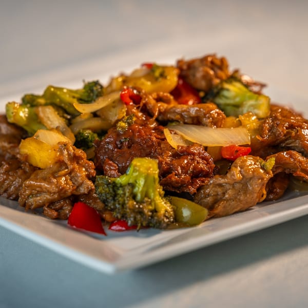 Close-up of Caribbean beef stir-fry with broccoli, onions, and red peppers on a white plate.
